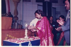 Mrs. Arigapudi Krishna-Kumari lighting the lamp at an event. Ln AVK in the background